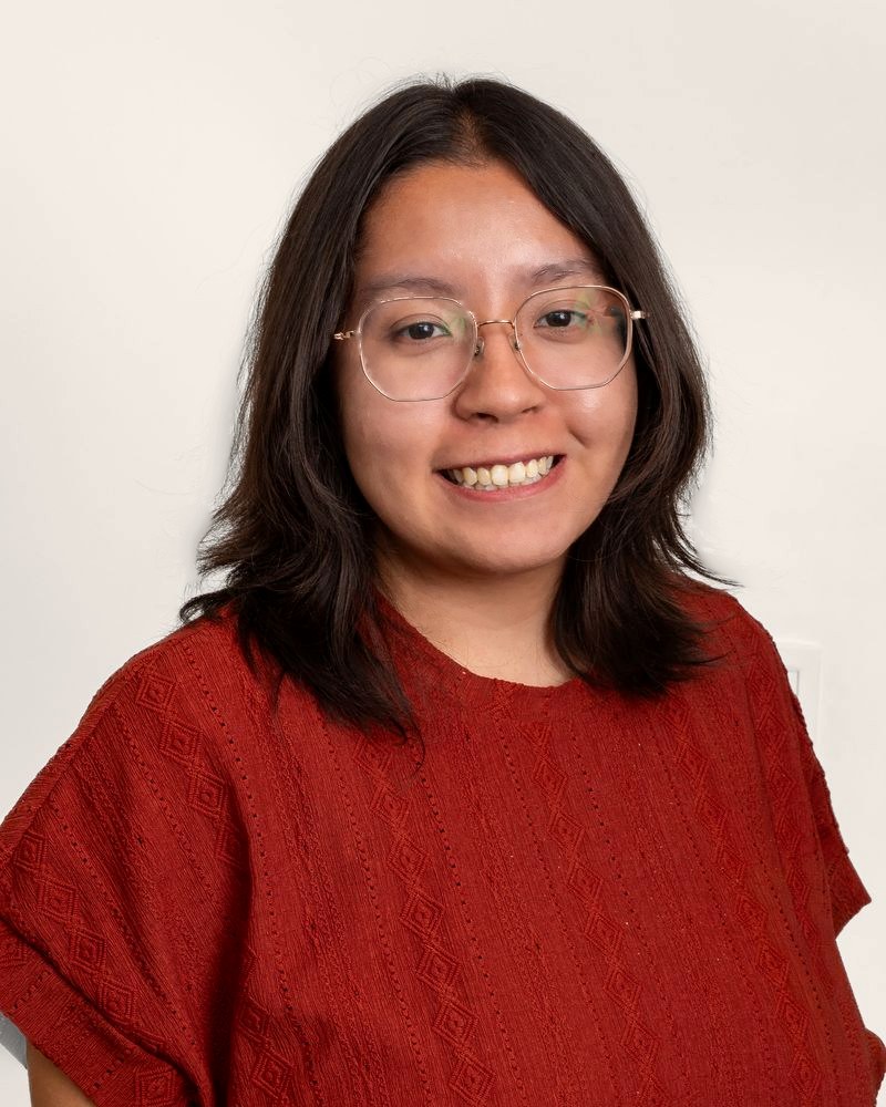 Amanda Kubo, smiling, wearing glasses and a rust-red top